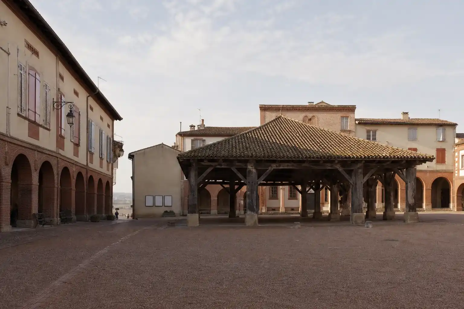 Place d’une bastide médiévale au nord-ouest de Toulouse, arcades de brique et grande halle couverte à charpente de bois