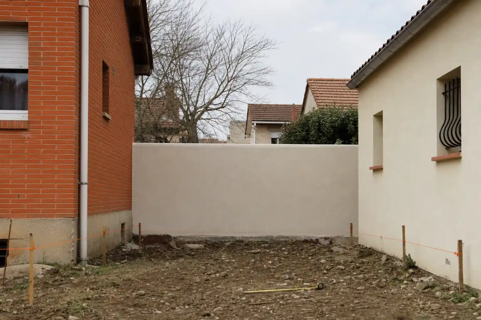 Petite parcelle enserrée entre deux maisons dans une commune de l’ouest toulousain, recul mesuré au ruban et marqué par des piquets