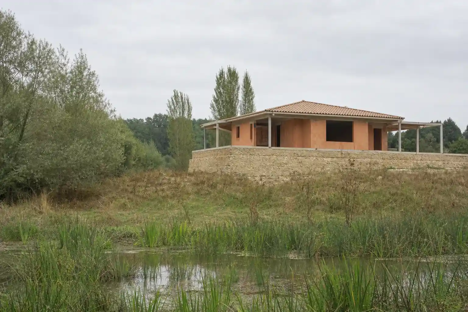 Terrain dans la vallée de la Lèze au sud de Toulouse, saules et prairie humide, maison en construction sur une plateforme de remblai surélevée