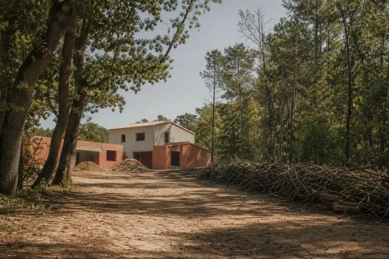 Terrain en lisière d’une grande forêt de chênes et de pins au nord-ouest de Toulouse, maison en construction sous les arbres, andains de broussailles en limite