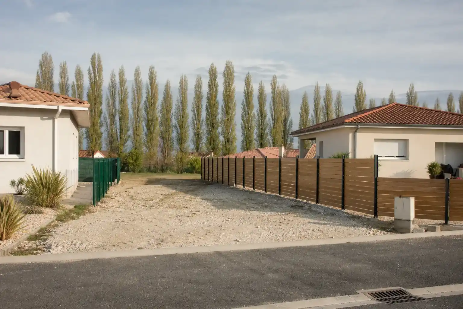 Rue résidentielle de la plaine alluviale au sud de Toulouse, maisons basses enduites, rideau de peupliers marquant la Garonne