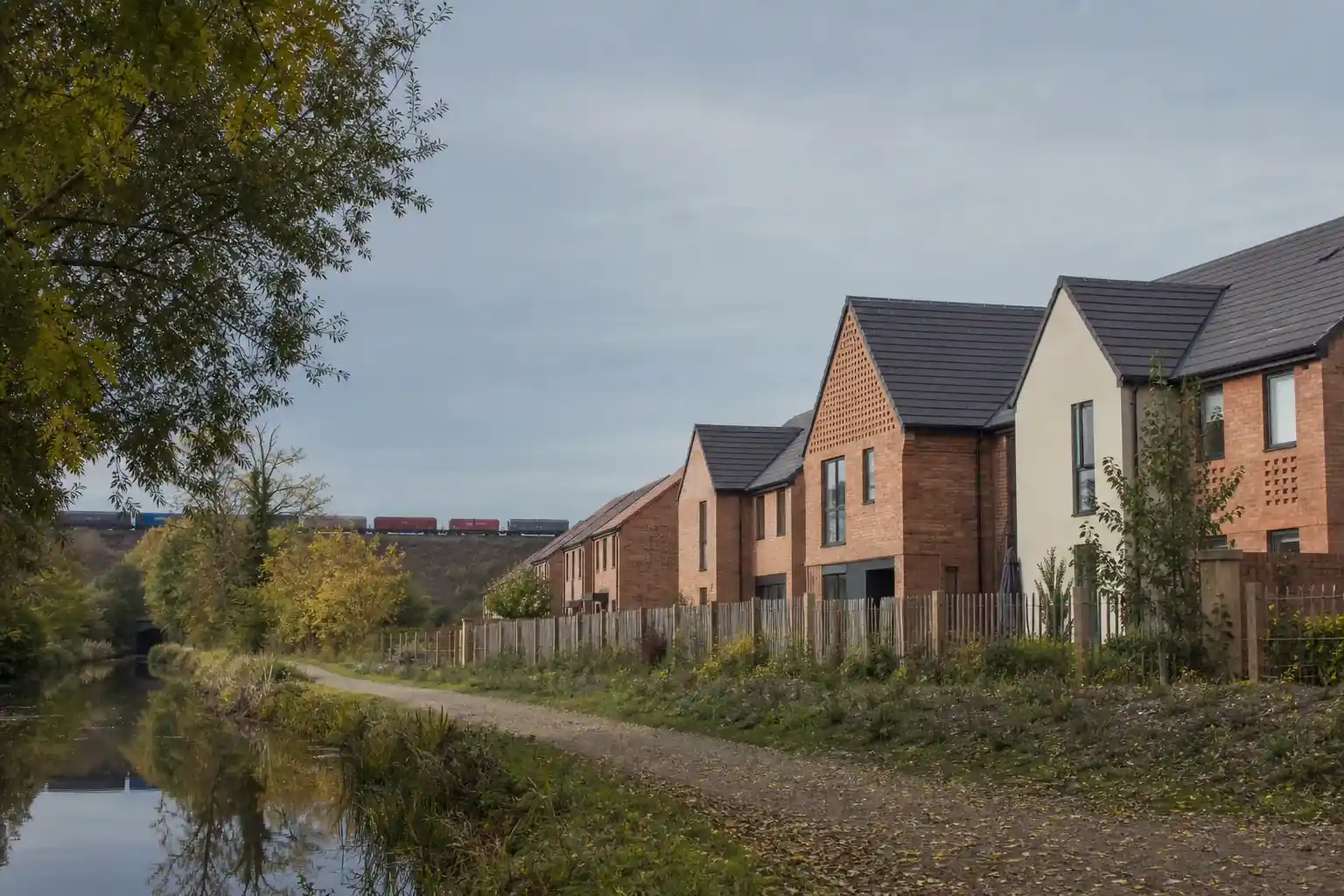 Frange résidentielle d’une commune du nord toulousain le long d’un canal bordé d’arbres, chemin de halage et maisons neuves derrière une clôture basse